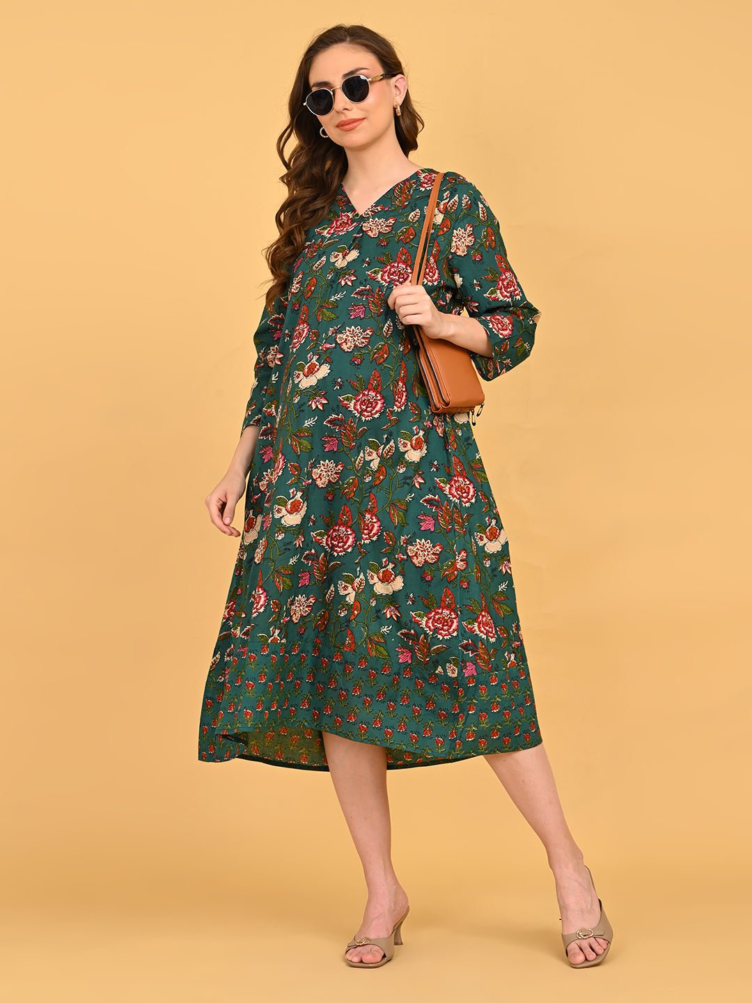Model styling green floral maternity midi dress with sunglasses, tan shoulder bag, and beige heels.