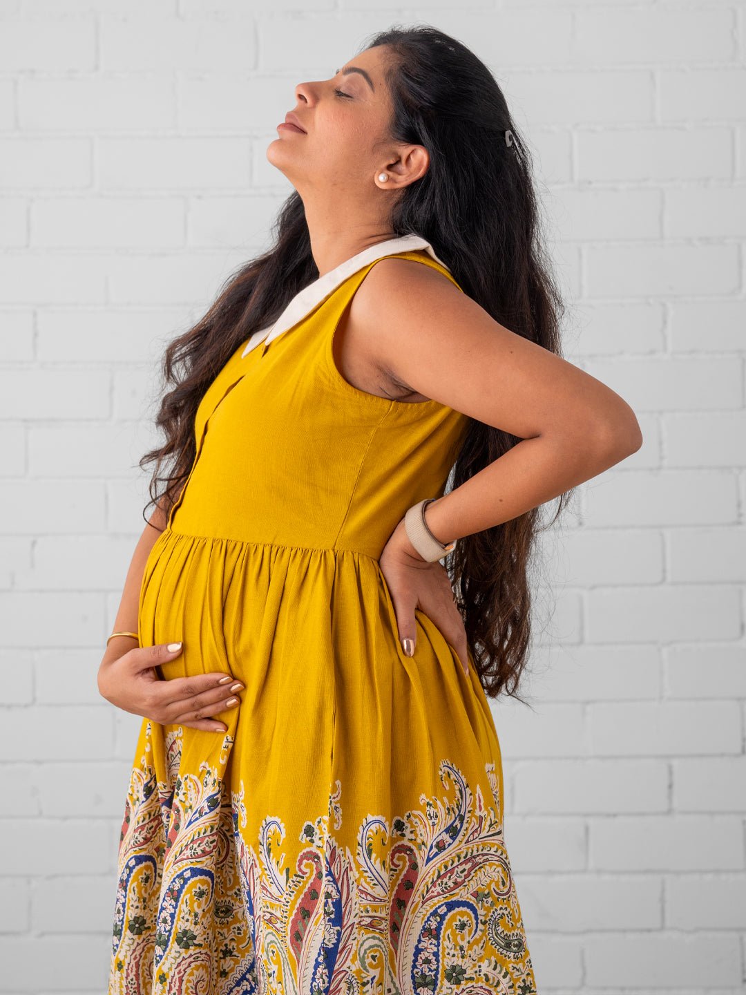 Pregnant woman in yellow maternity dress relaxing and holding baby bump – The Mom Store