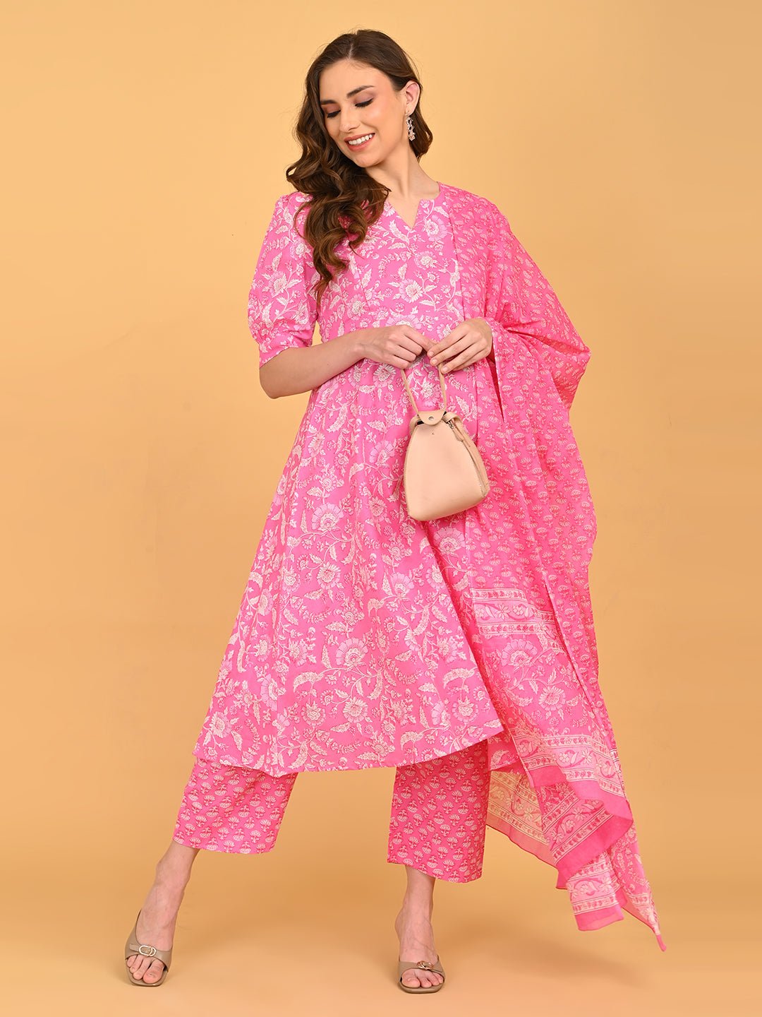 Model styling pink maternity kurta set with dupatta and beige handbag for festive wear.