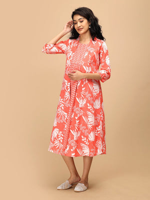 Model wearing a peach printed maternity and nursing dress layered with a matching open-front shacket, standing against a beige background.