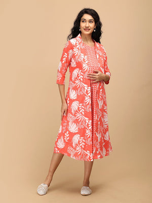 Model wearing a peach printed maternity and nursing dress layered with a matching open-front shacket, standing against a beige background.