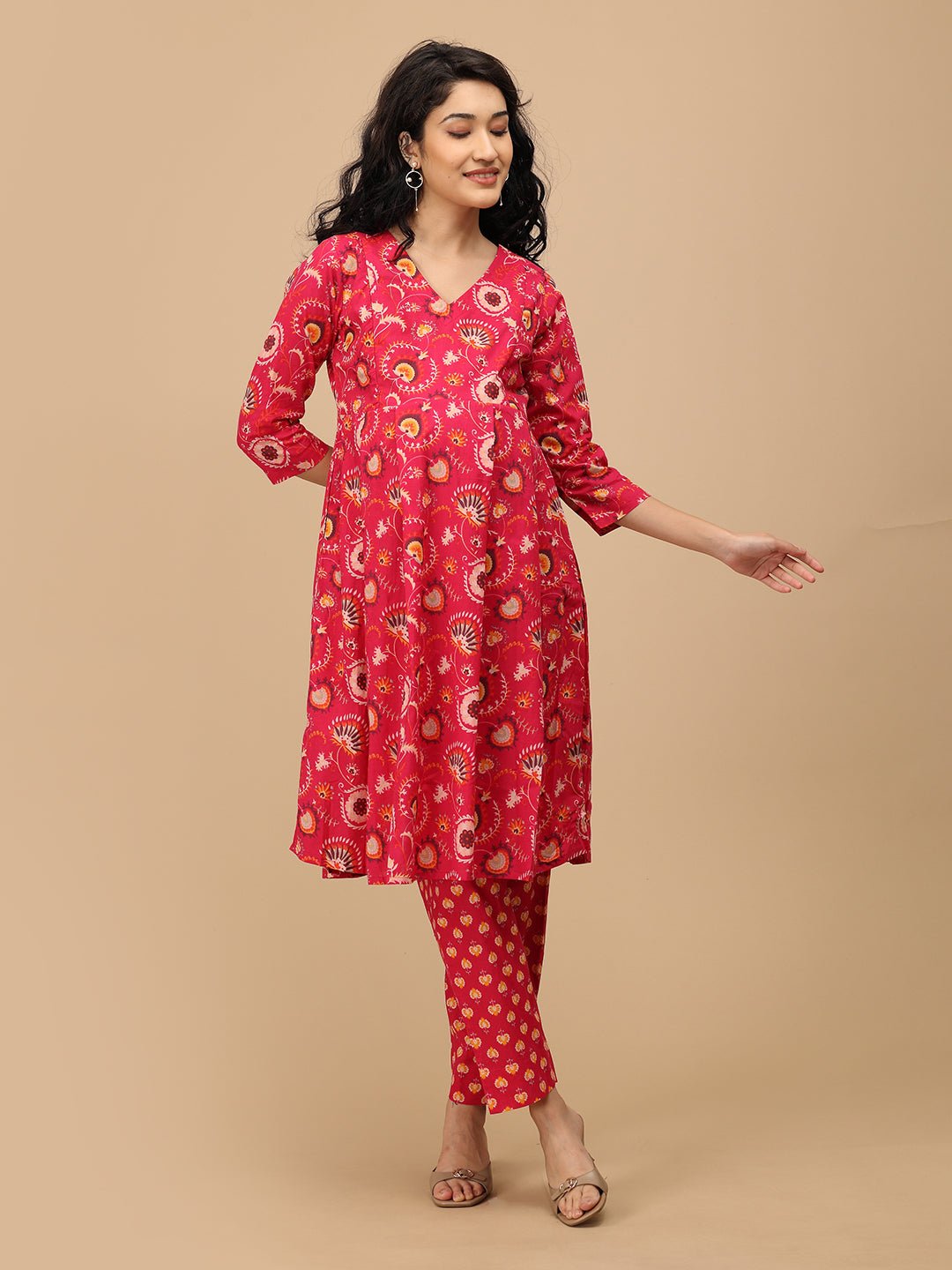 Pregnant woman wearing a bright pink printed maternity kurta with three-quarter sleeves and matching straight pants, gently holding her bump.