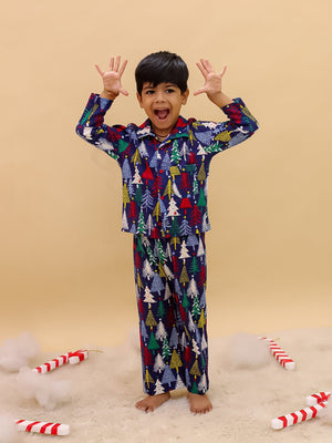 Playful boy wearing The Mom Store Silent Night Christmas Kids Pajama Set, posing with raised hands and excited expression, surrounded by candy cane props on a soft rug.