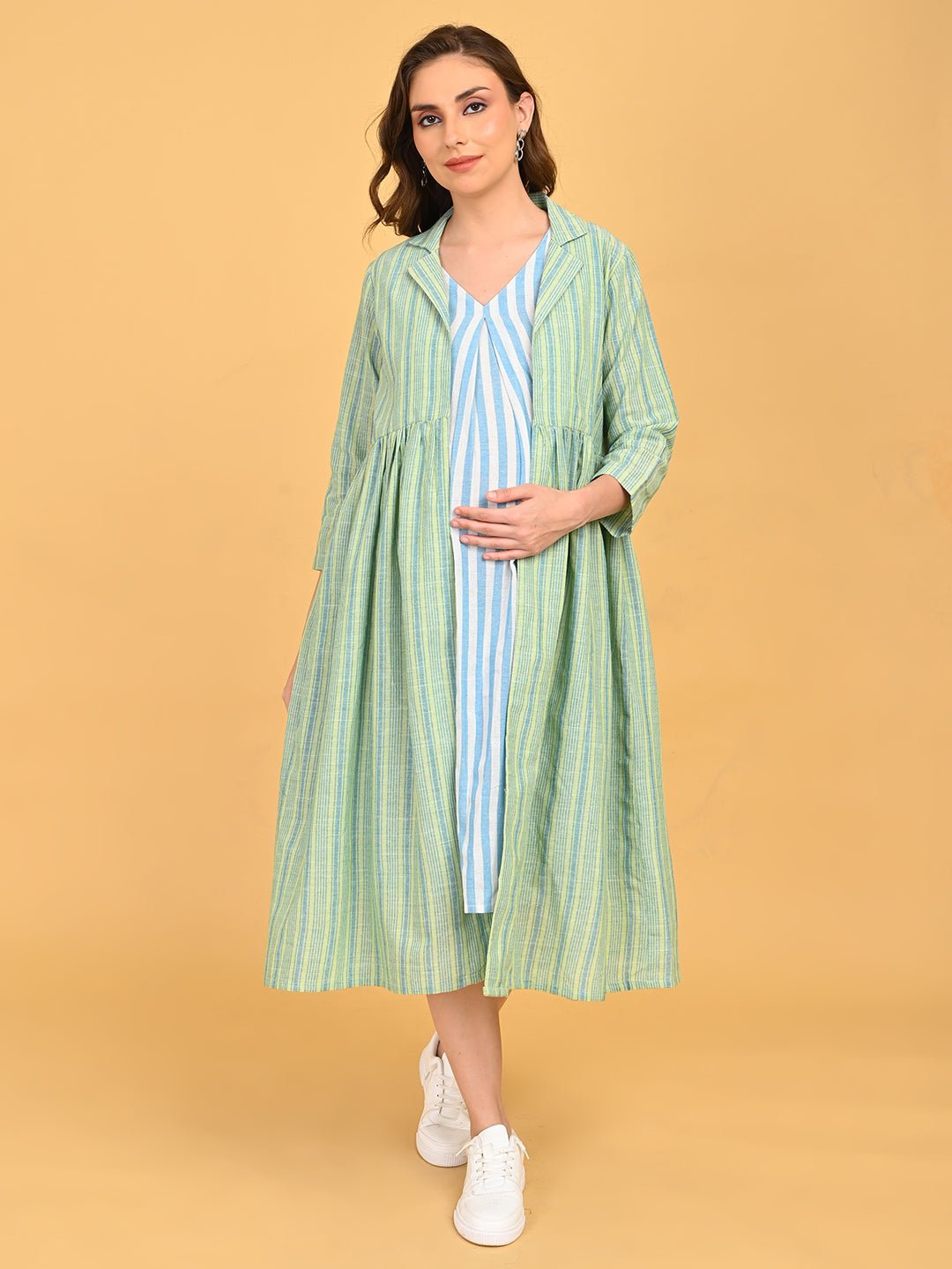 Pregnant model wearing striped maternity dress layered with green striped long shacket, styled with white sneakers.