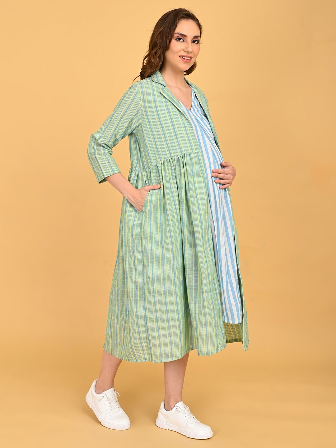 Side view of pregnant model in striped maternity dress and green shacket highlighting bump-friendly fit.
