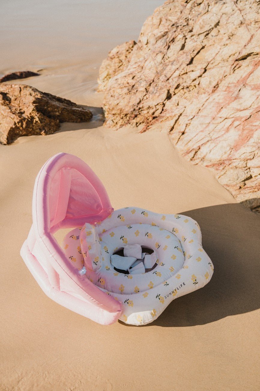 Pink and white shell-shaped product on a sandy beach with rocks.