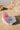 Pink and white shell-shaped product on a sandy beach with rocks.