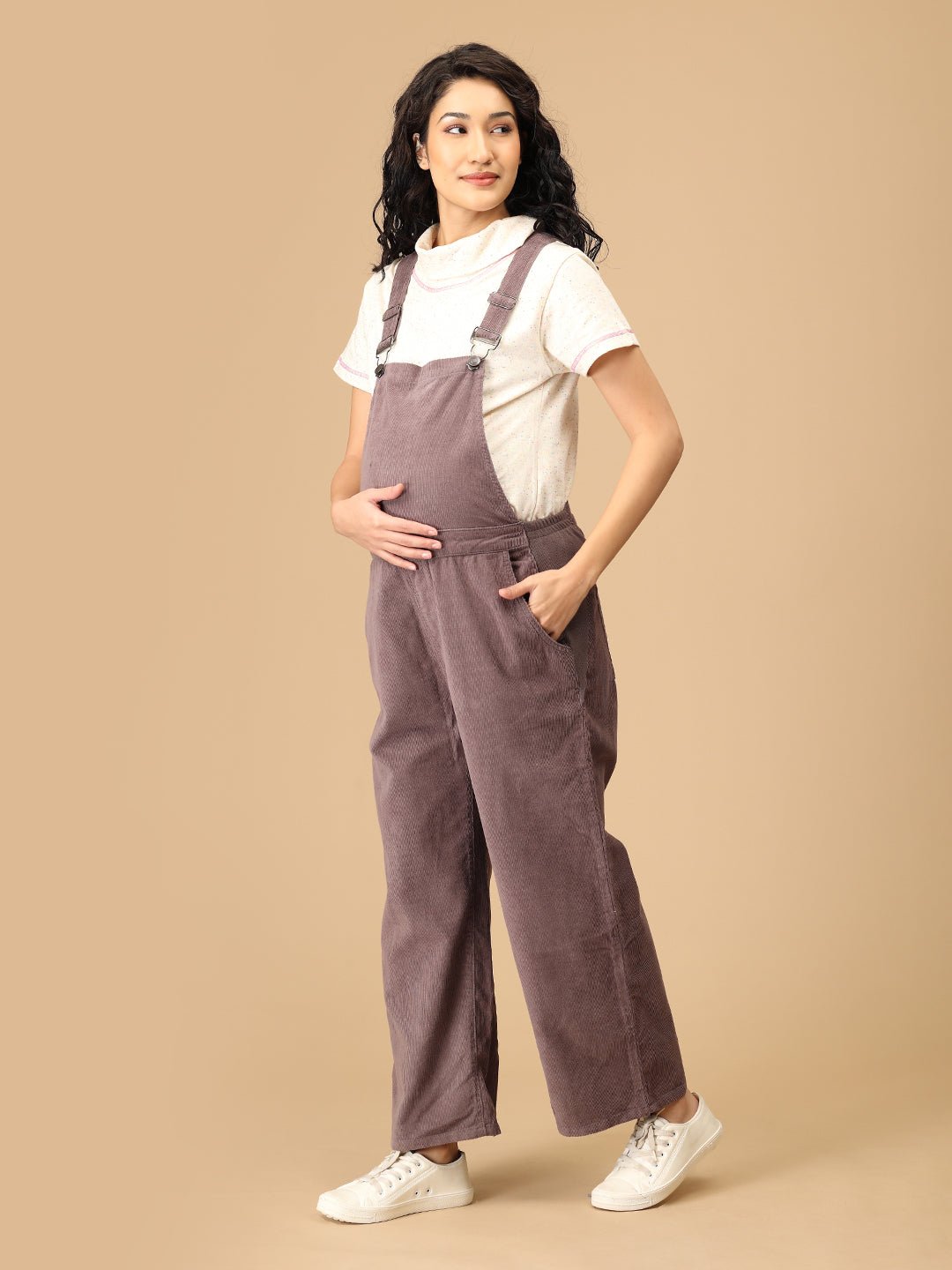Side pose wearing The Mom Store taupe corduroy maternity dungaree with bump-friendly fit.