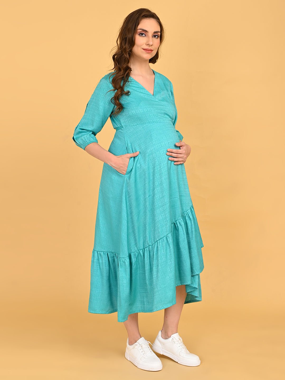 Turquoise Temptation Maternity Wrap Dress front view with hands in pockets, showcasing textured fabric and ruffle hem detail.